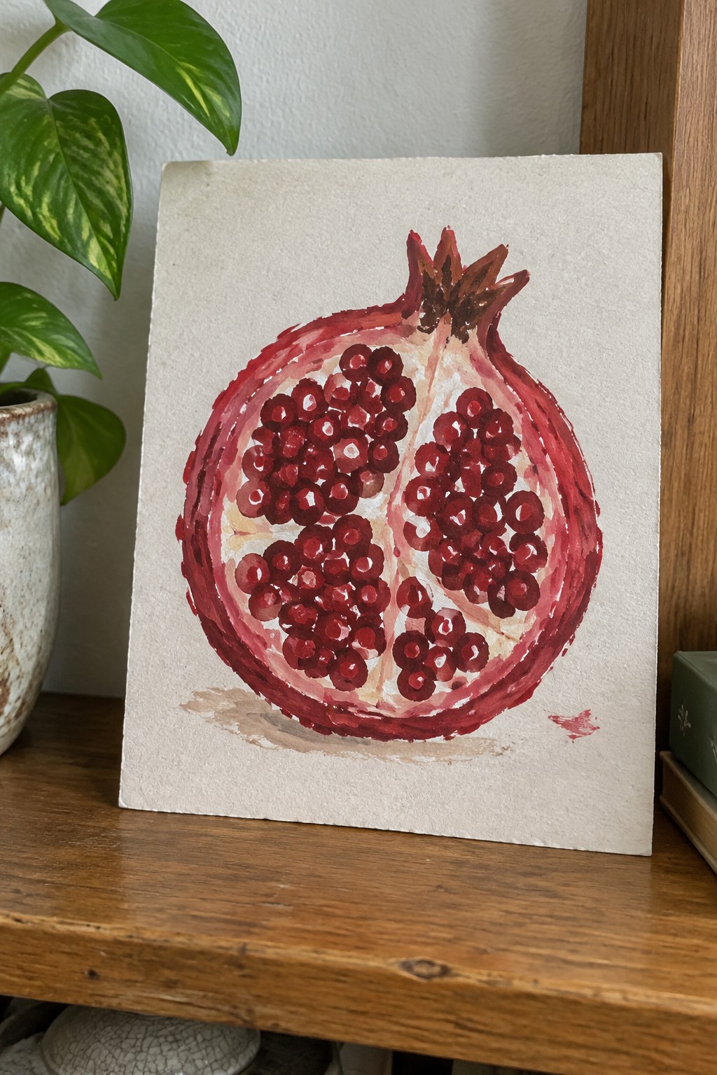 Watercolor painting of halved pomegranate with red seeds on textured paper.
