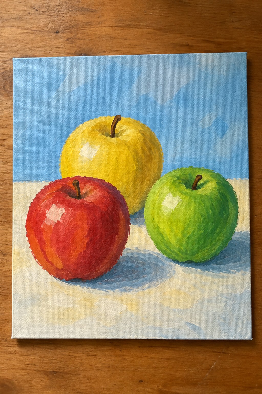 Still life painting of red, yellow, and green apples on white surface with blue background.