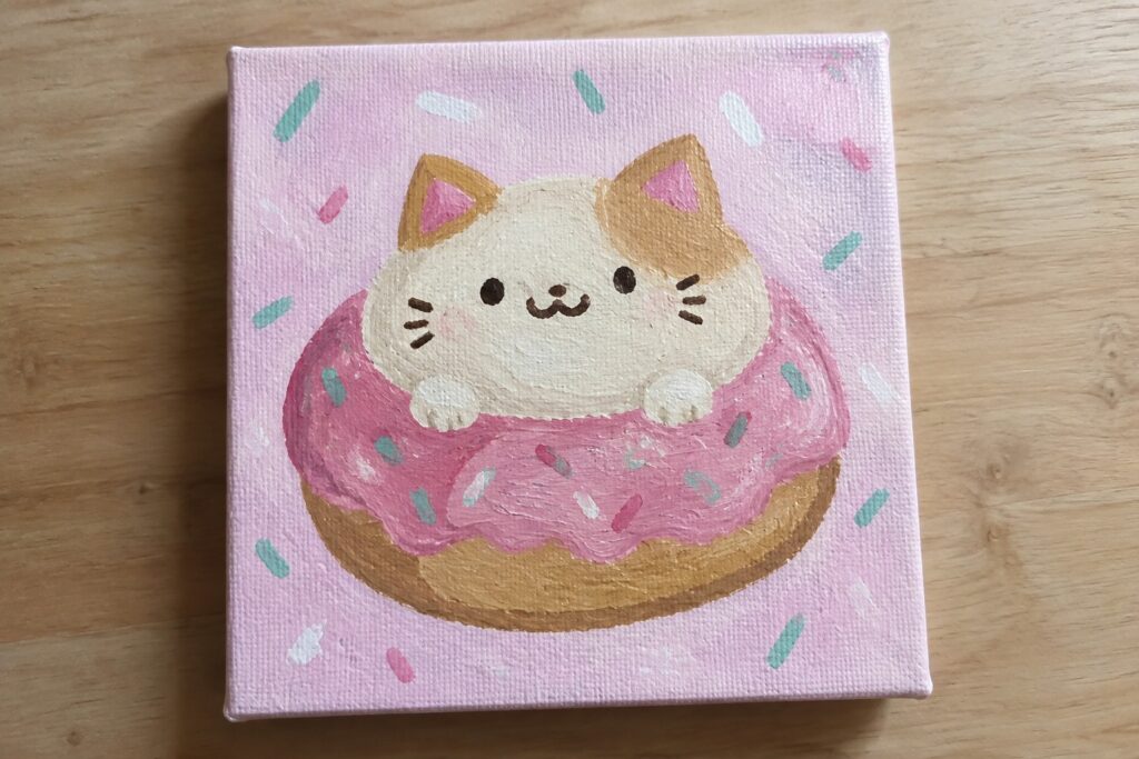 A small square canvas shows a white and brown striped cat with pink cheeks sitting on a pink frosted donut against a mint background with pink dots.