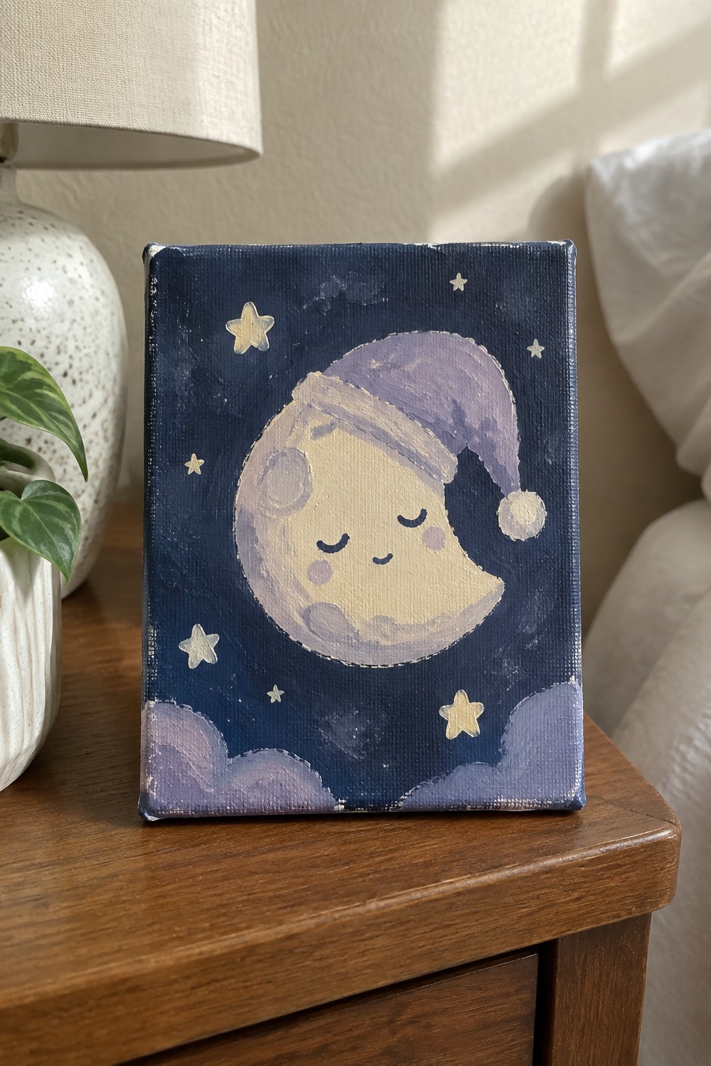 Crescent moon in purple nightcap on dark blue starry canvas atop wooden table.