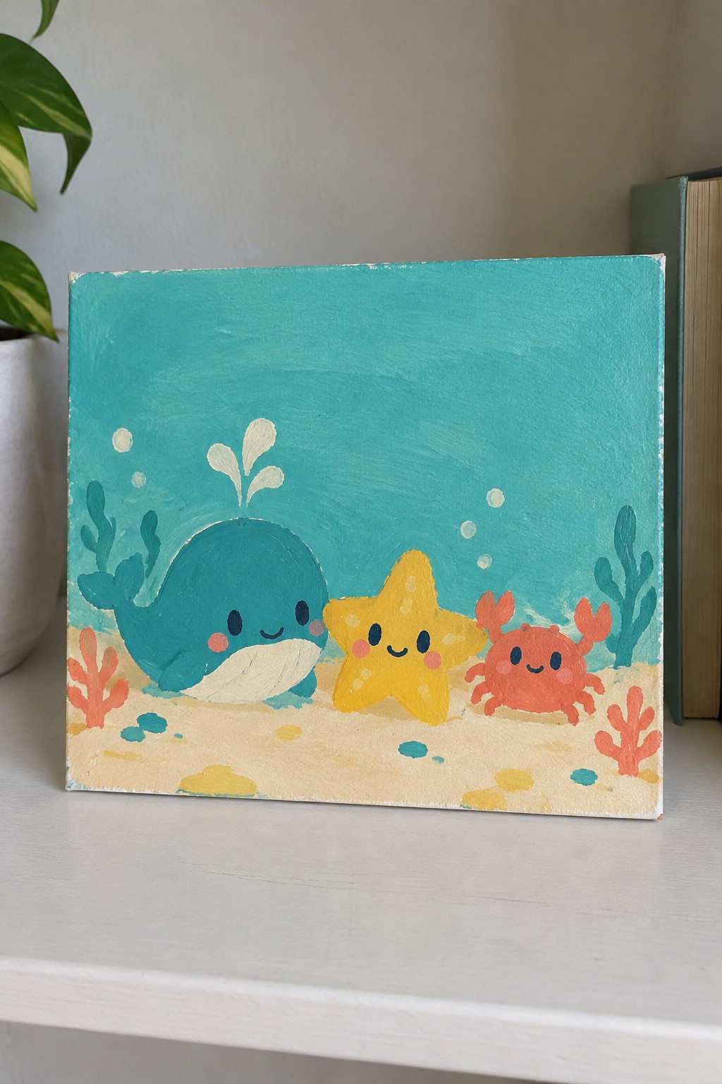 Cute acrylic painting of smiling teal whale, yellow starfish, and red crab on sandy seabed with coral