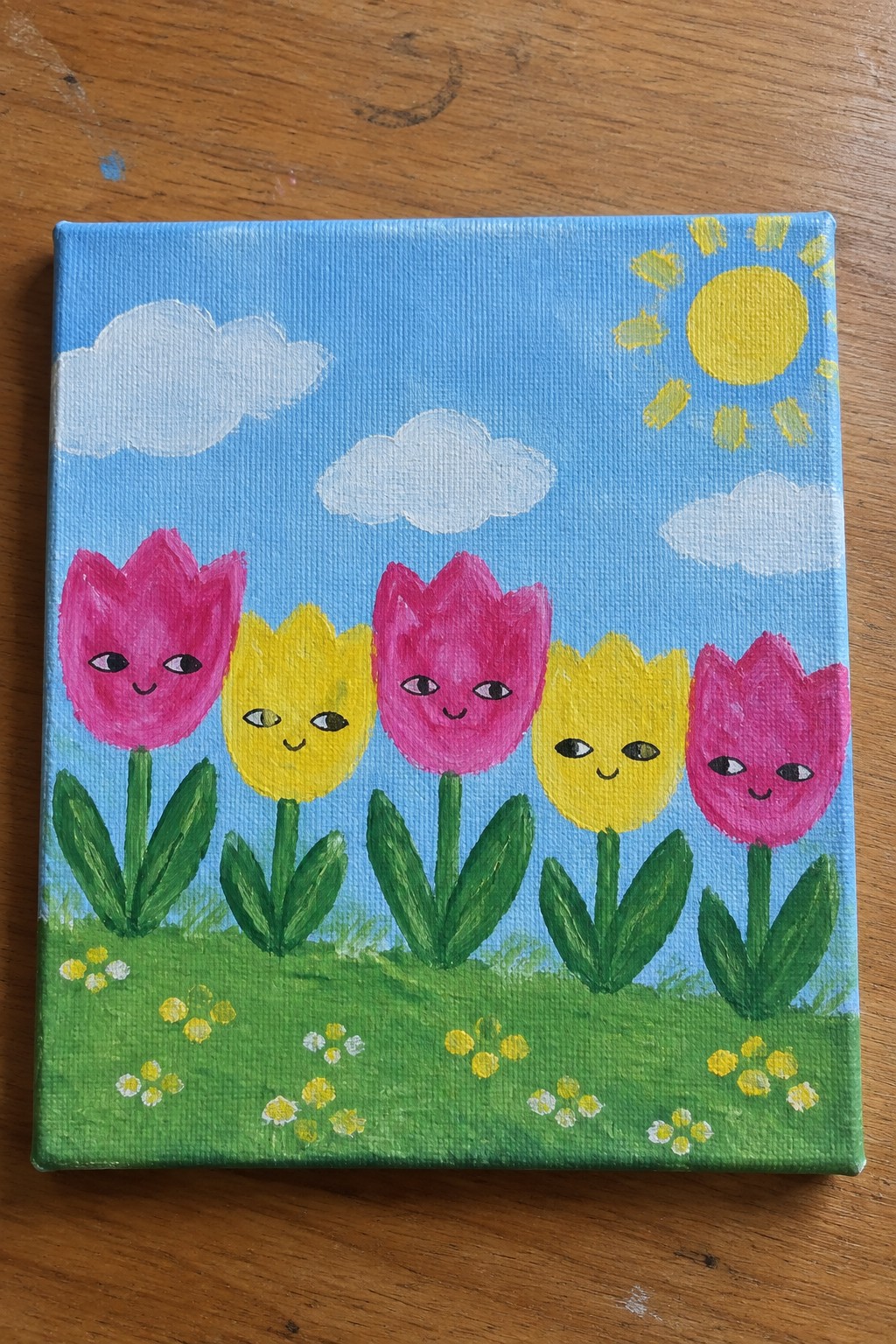 Five pink and yellow tulips with cute faces on green grass under sunny blue sky
