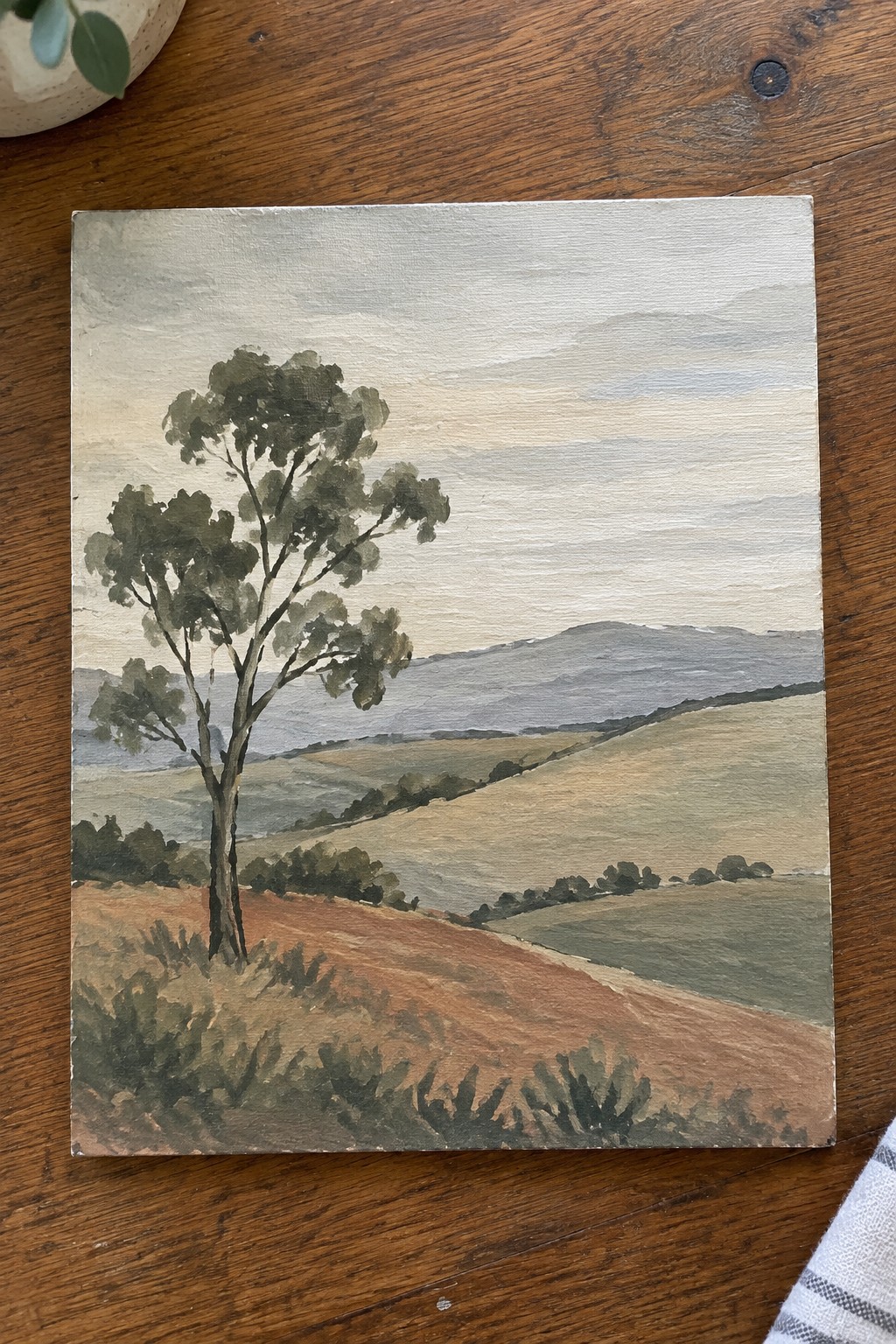 Watercolor landscape painting of lone tree amid rolling hills and fields under cloudy sky