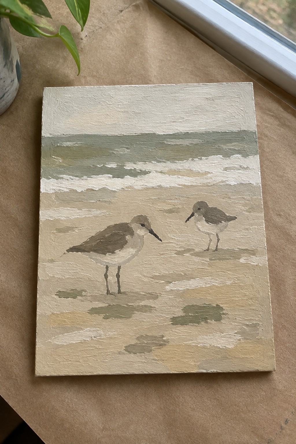 A small rectangular canvas shows two brown and white shorebirds standing on a sandy beach with soft ocean waves and a pale sky above.