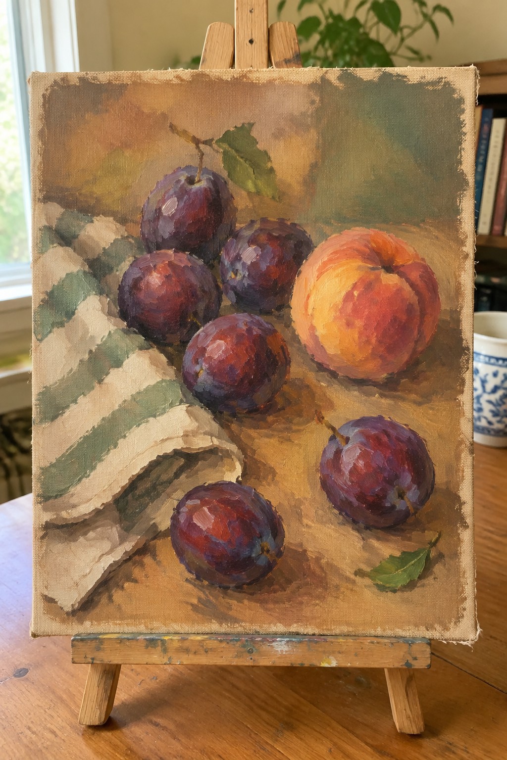Still life oil painting of purple plums, peach, and striped cloth on easel