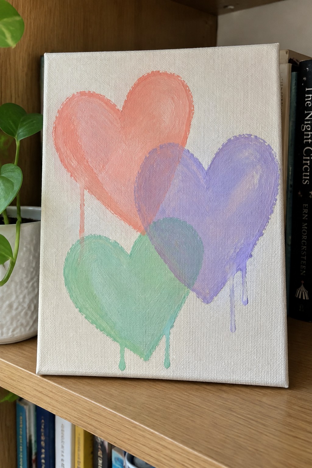 Three overlapping hearts in coral, purple, and green with paint drips on canvas