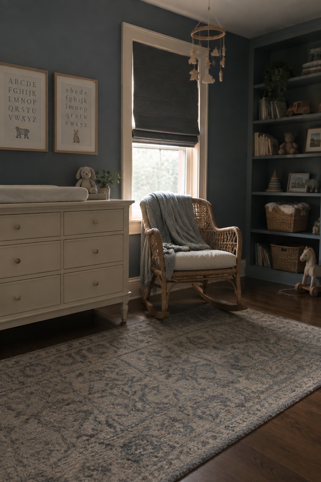A nursery featuring deep blue-gray walls with white trim, a woven rocking chair, and a soft patterned rug.
