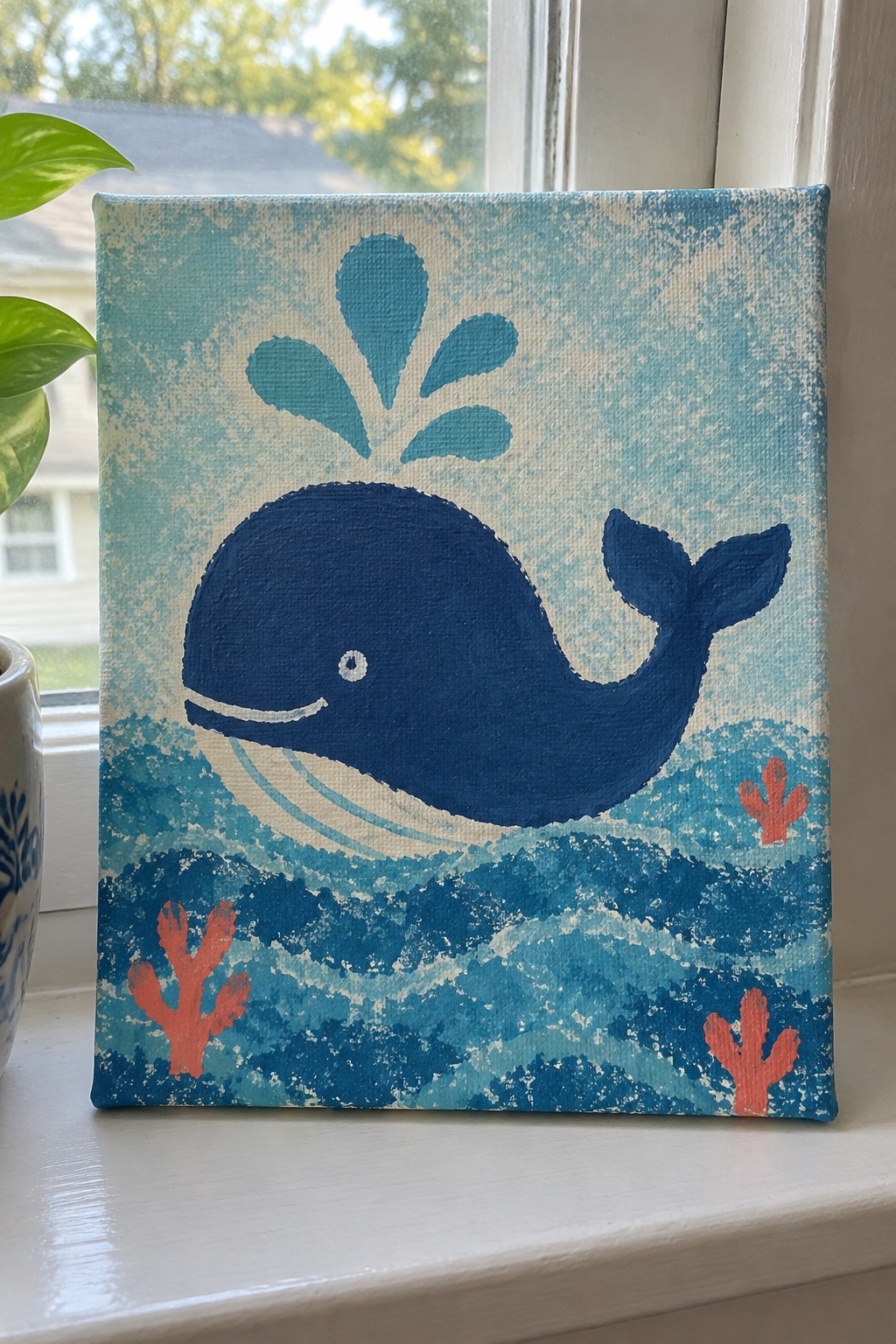 Blue whale painting on canvas with teal spout, wavy ocean, and red coral accents.