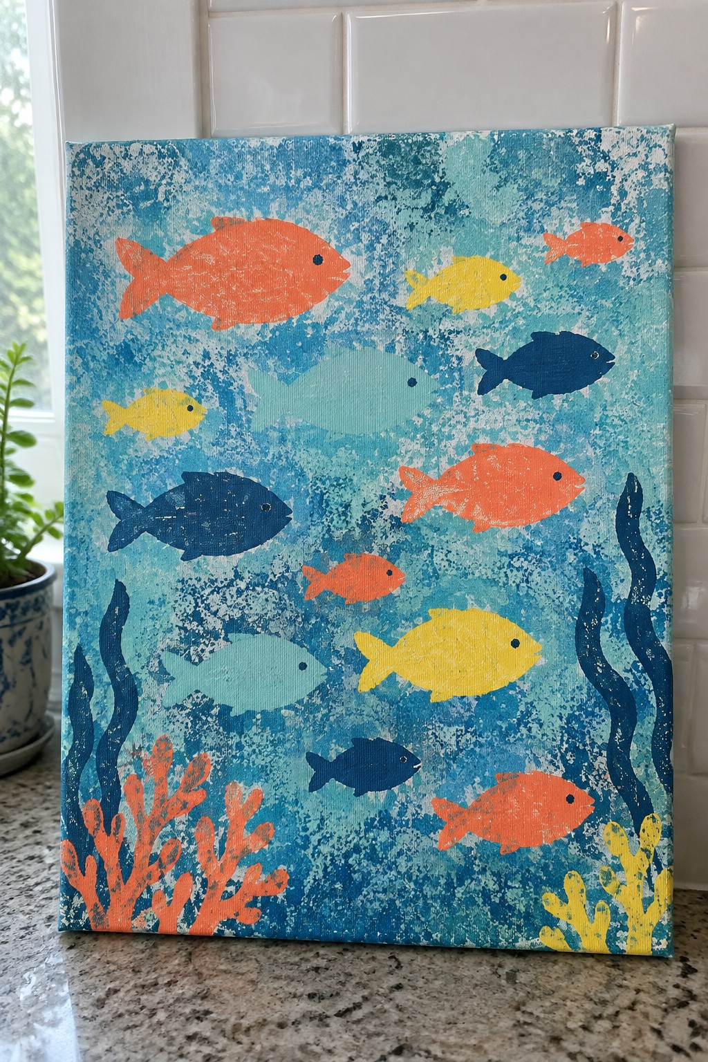 A rectangular canvas displays multiple colorful fish in orange, yellow, light blue, and dark blue against a textured blue and white background, with orange coral and yellow and blue seaweed painted at the bottom.