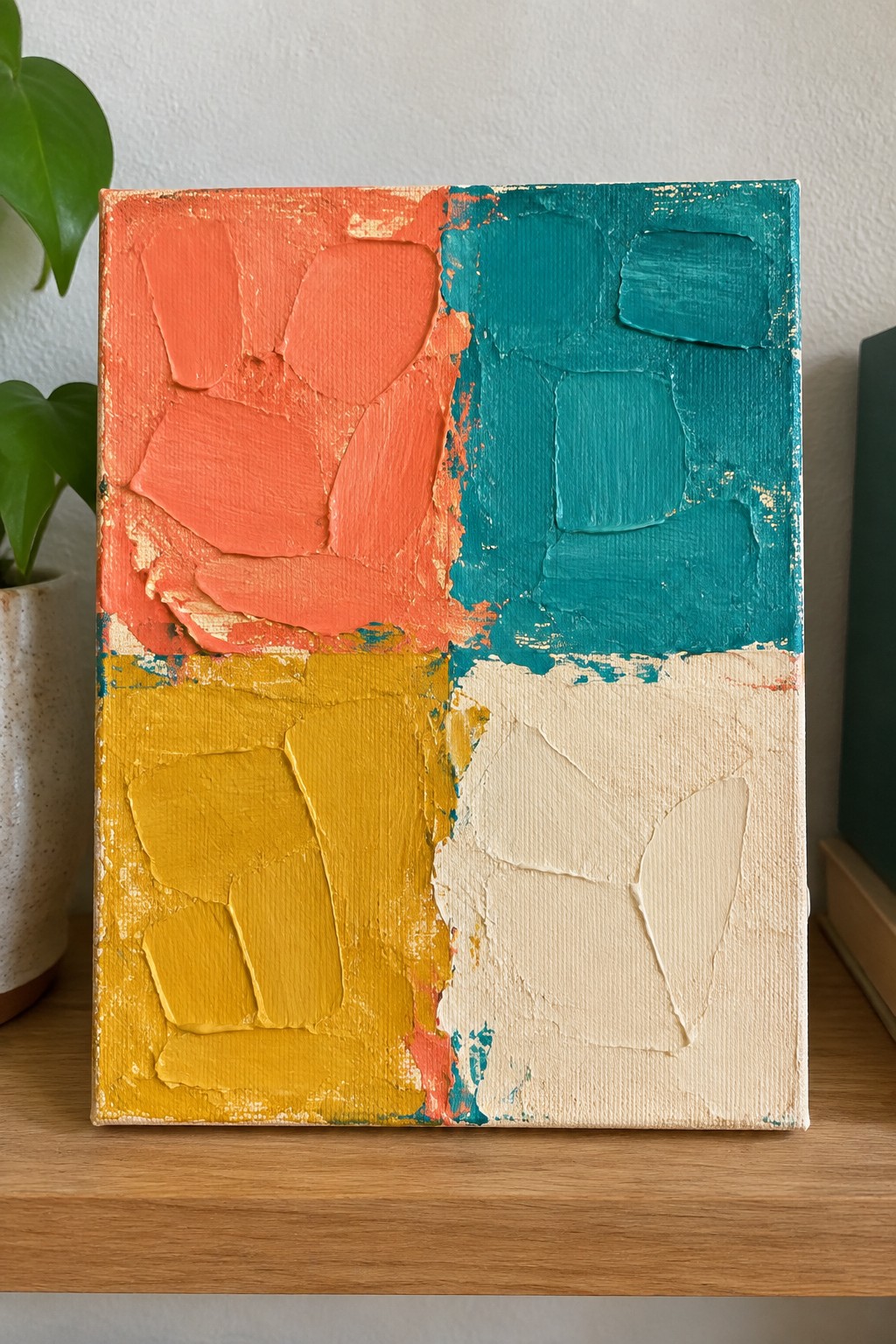 An abstract painting on a square canvas divided into four thickly painted quadrants of coral orange, teal, yellow, and off-white.