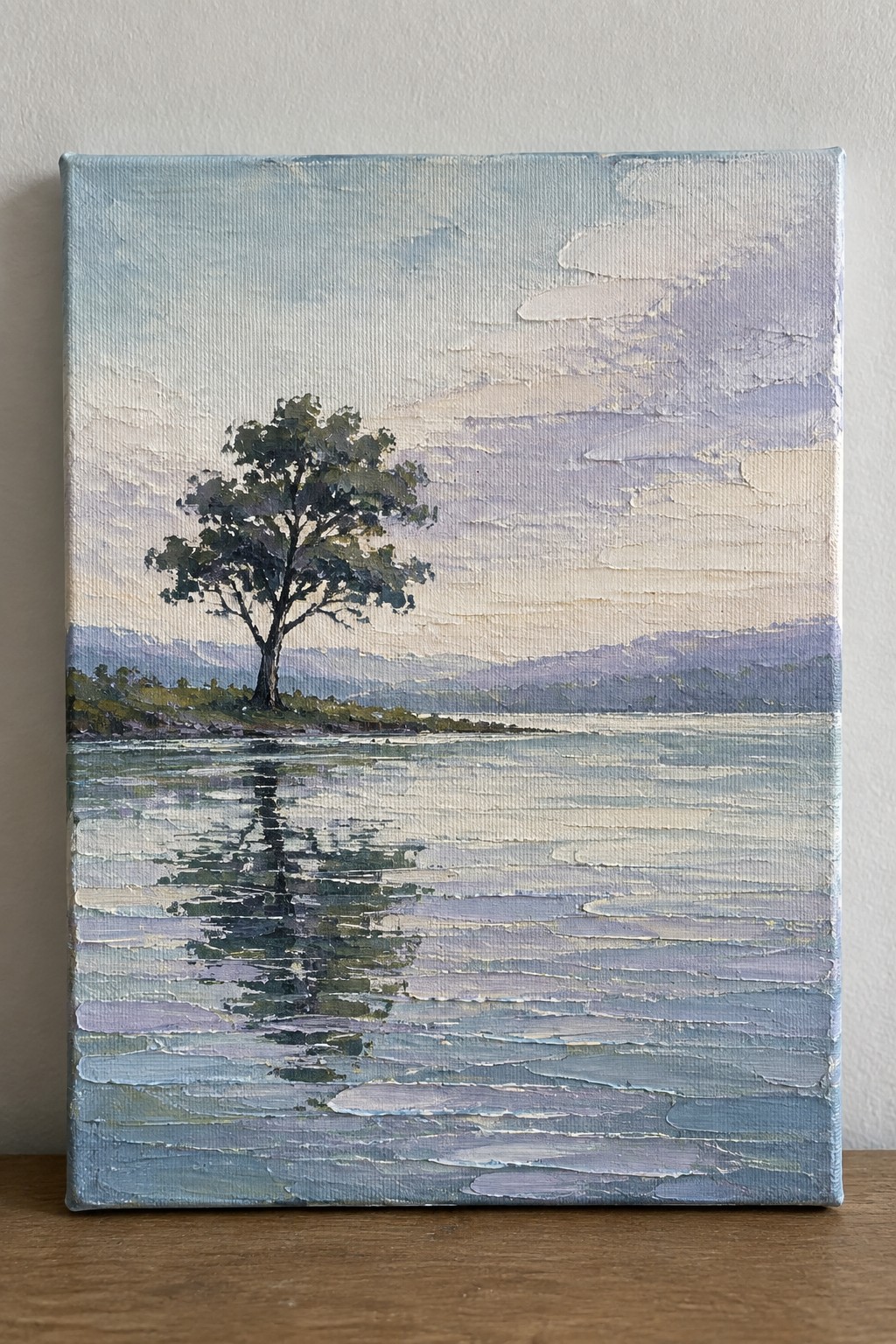 Serene landscape painting of lone tree reflected in calm blue waters with distant mountains