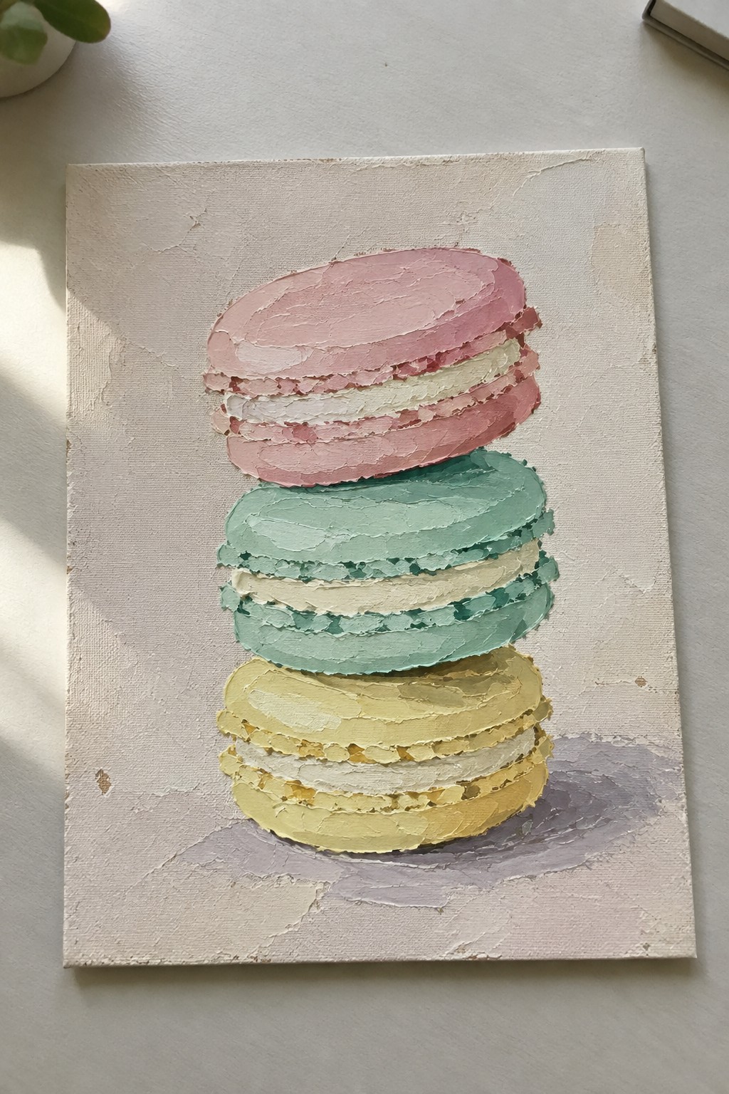 Impasto painting of stacked pink, mint green, and yellow macarons on canvas