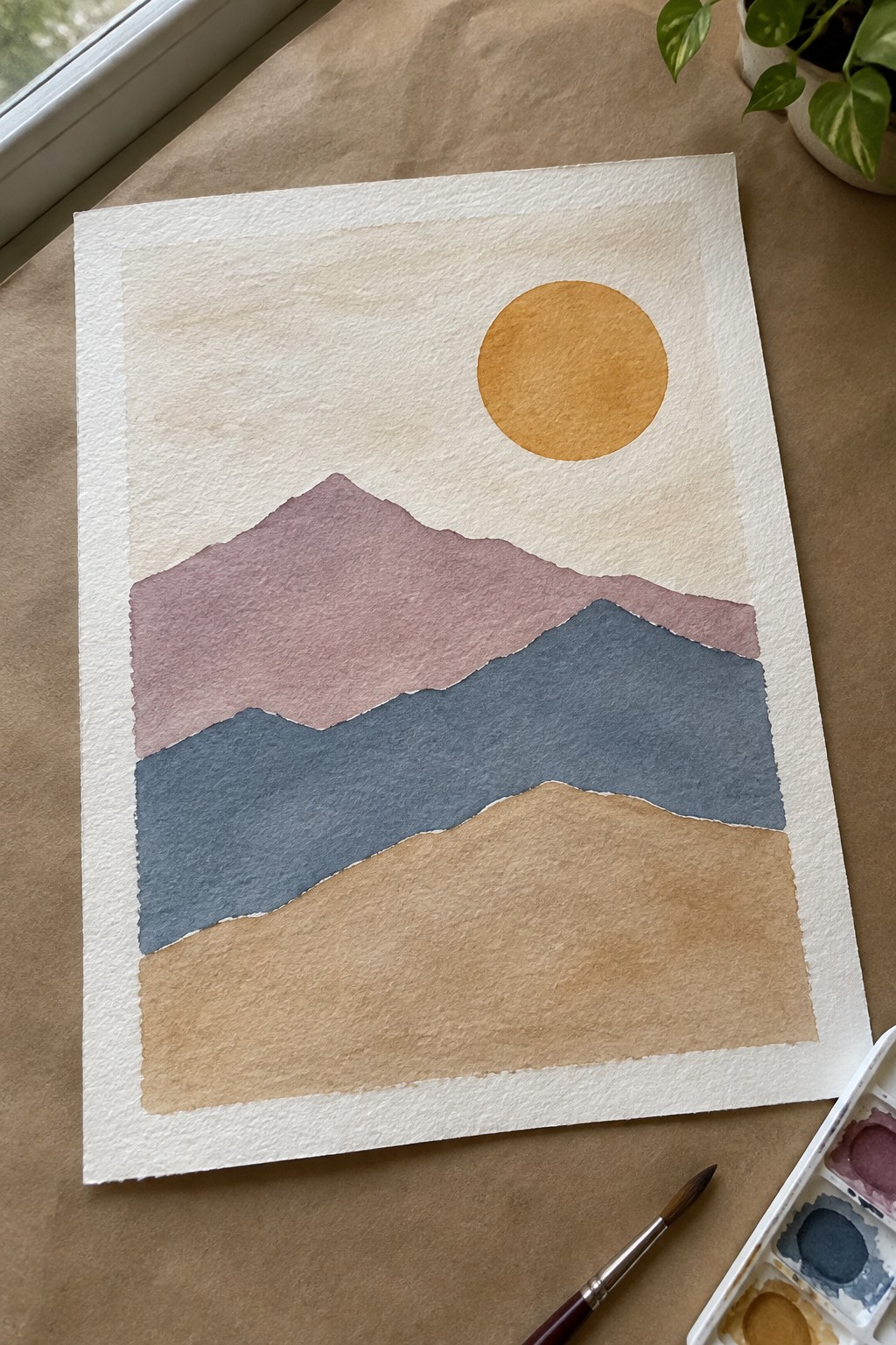 Watercolor landscape with layered purple, blue, and brown mountains, yellow sun, and paint supplies.