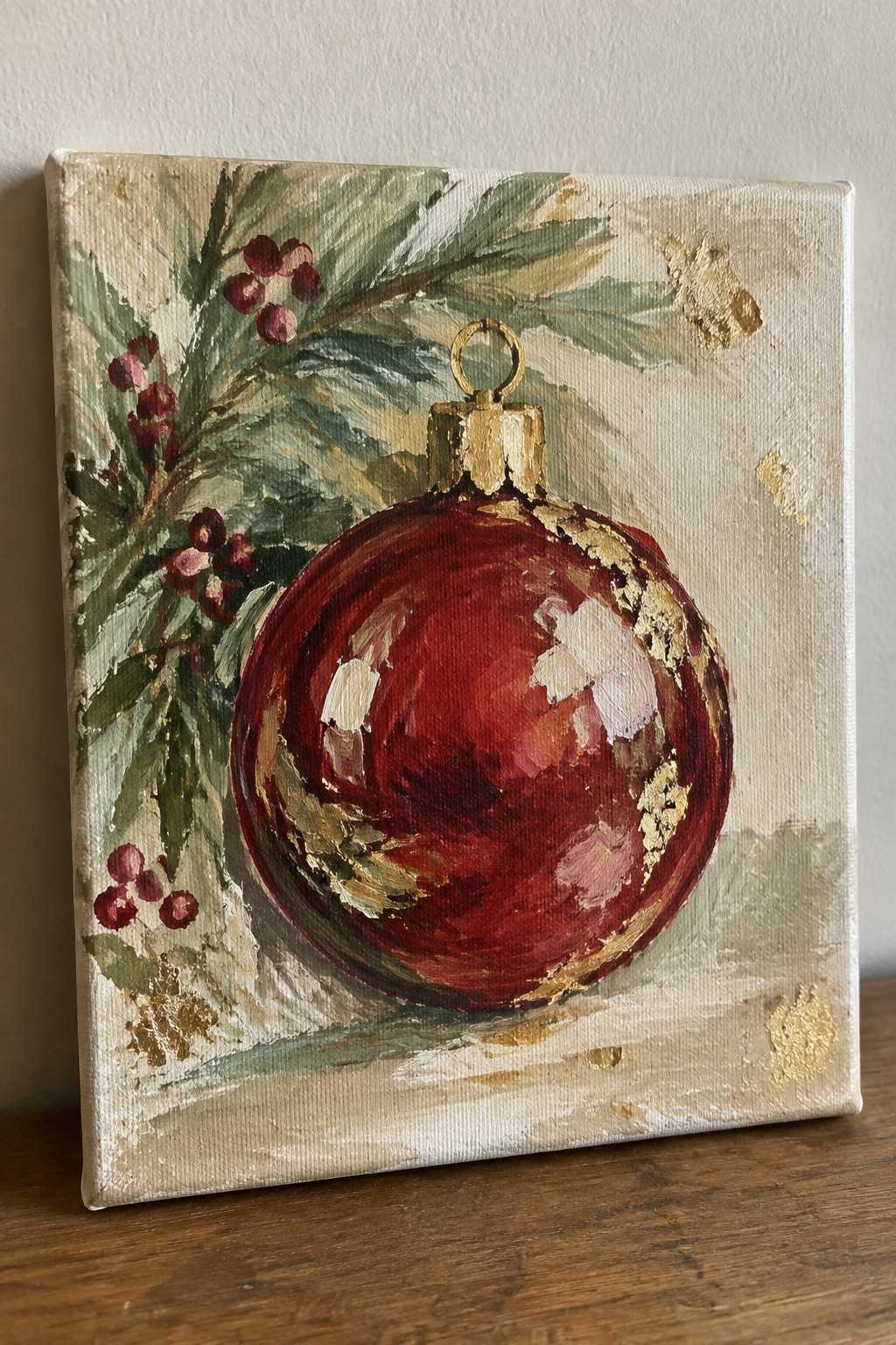 Red Christmas ornament with gold accents amid green foliage and red berries on canvas