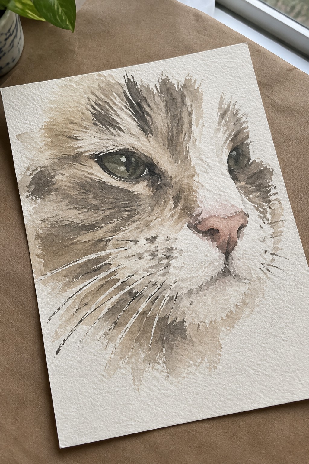 Watercolor of a cat's face in brown tones with green eye and whiskers on paper