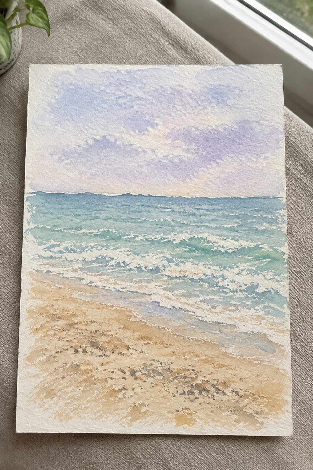 Watercolor of turquoise waves rolling onto beige sandy beach under pastel purple sky