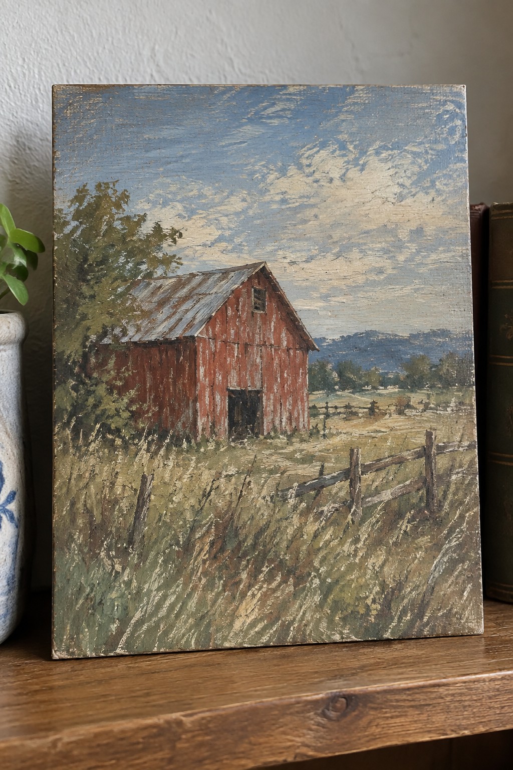 Weathered red barn with rusted roof in grassy field beside wooden fence under blue sky