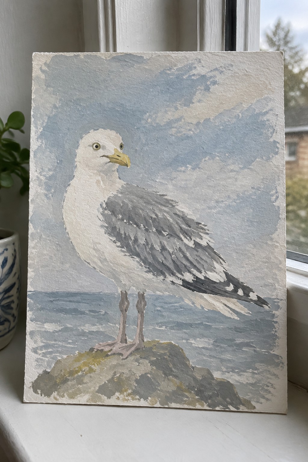 Watercolor seagull with gray wings and yellow beak on rock by blue sea