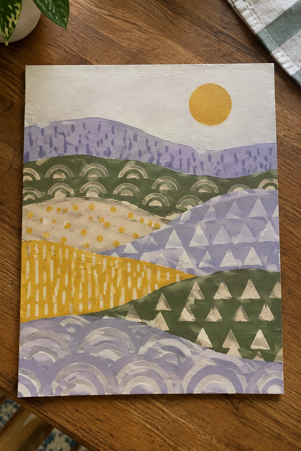 Abstract painting of layered hills with geometric patterns, yellow sun on wood