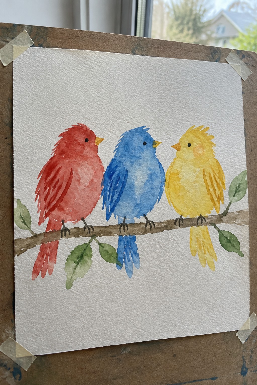 Watercolor painting of red, blue, and yellow birds perched on a leafy branch.
