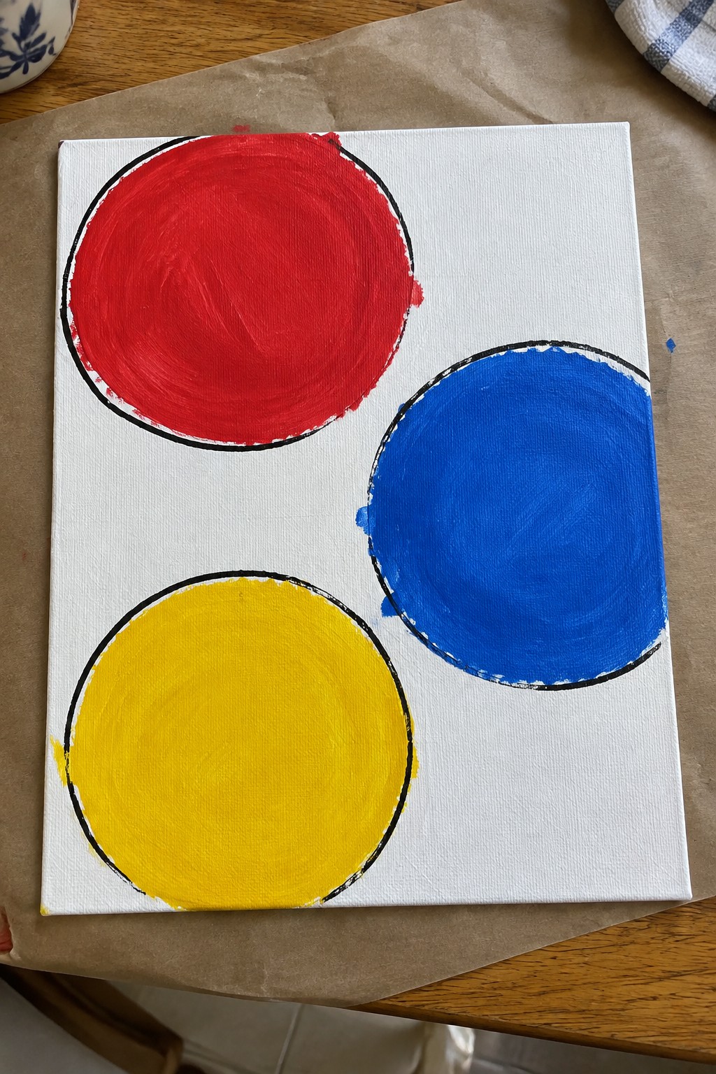 White canvas with red, blue, and yellow circles outlined in black on wooden table