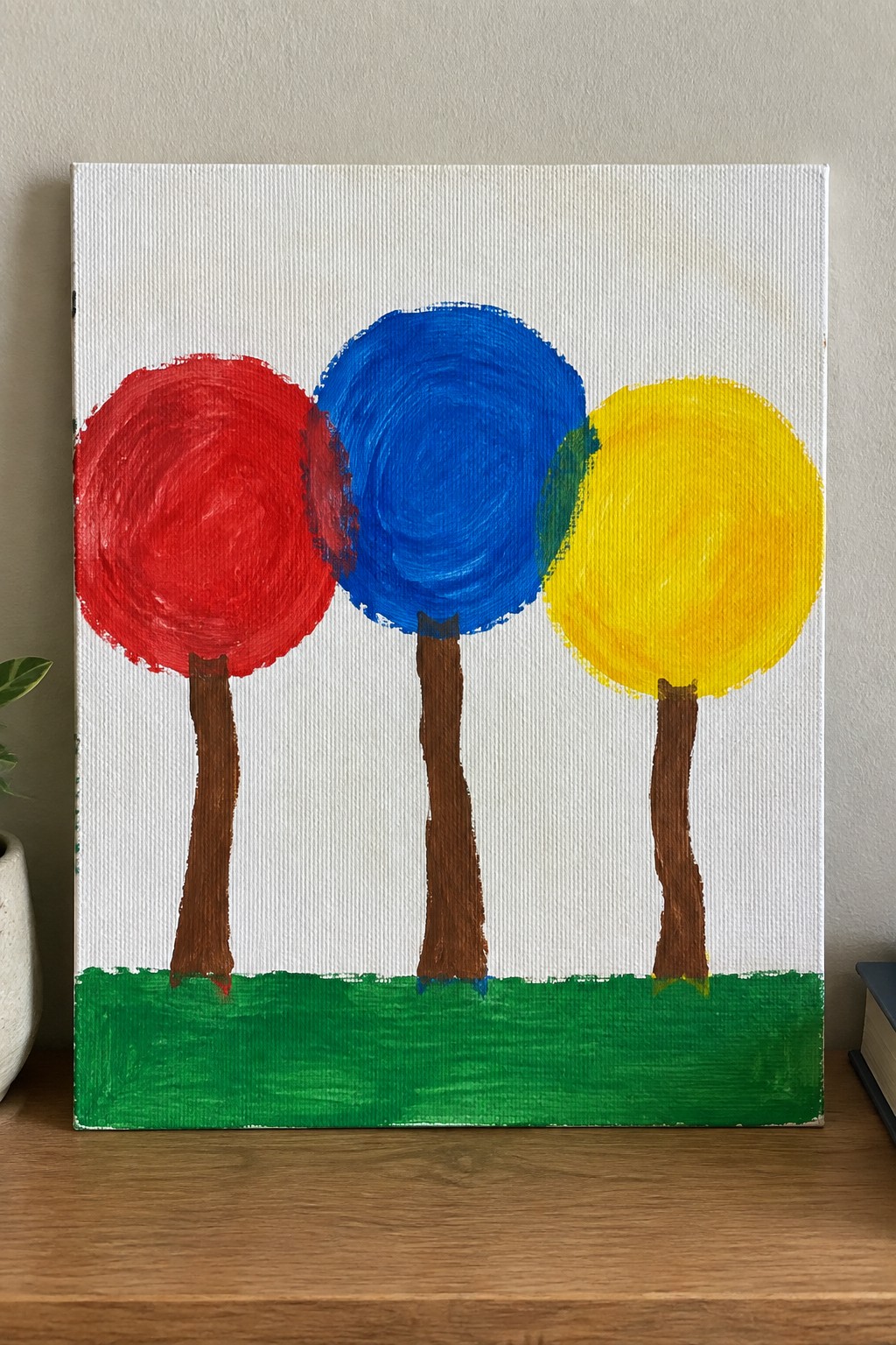 Three trees with red, blue, and yellow canopies on brown trunks above green grass.