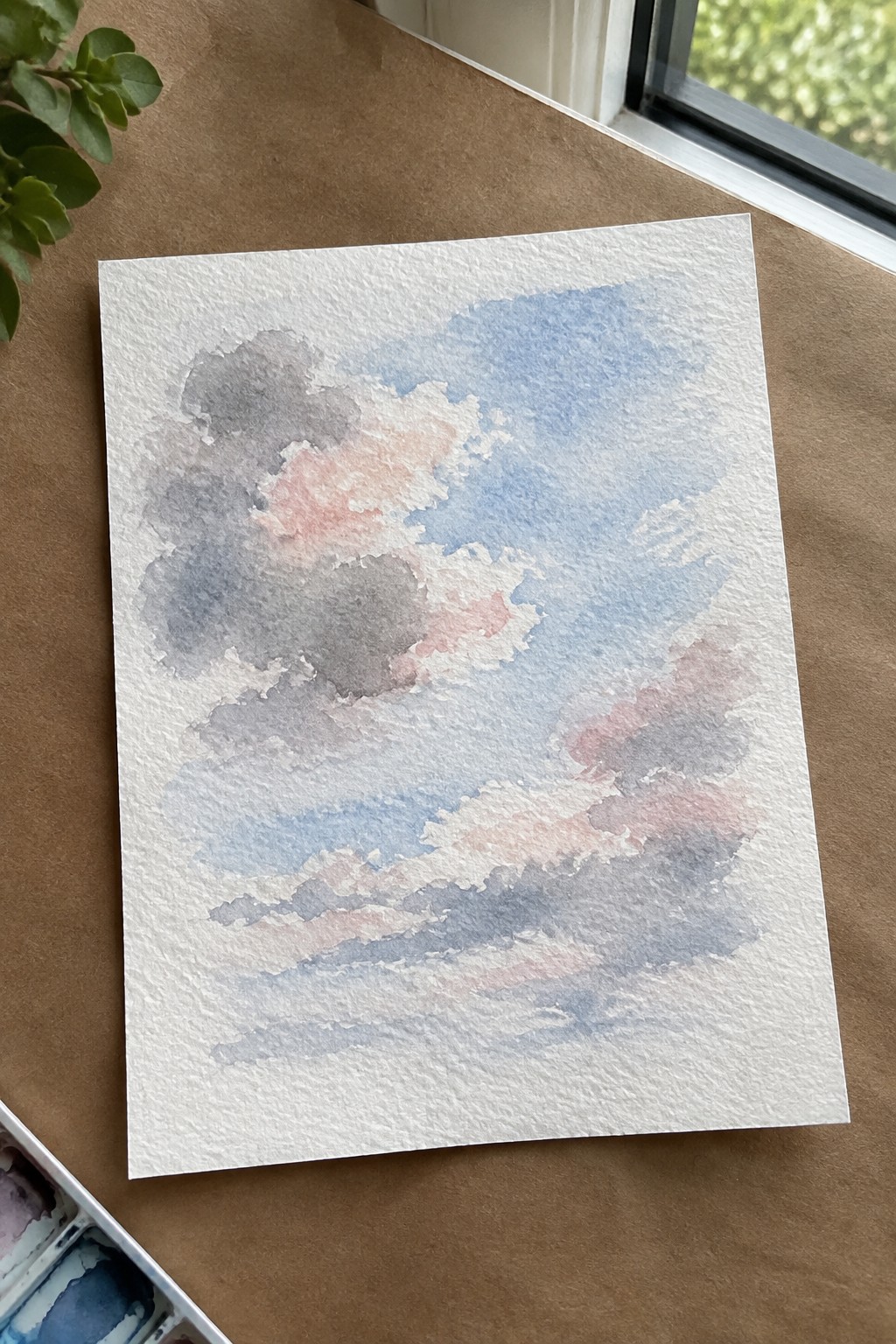 Watercolor sky with blue gray and pink clouds on textured white paper