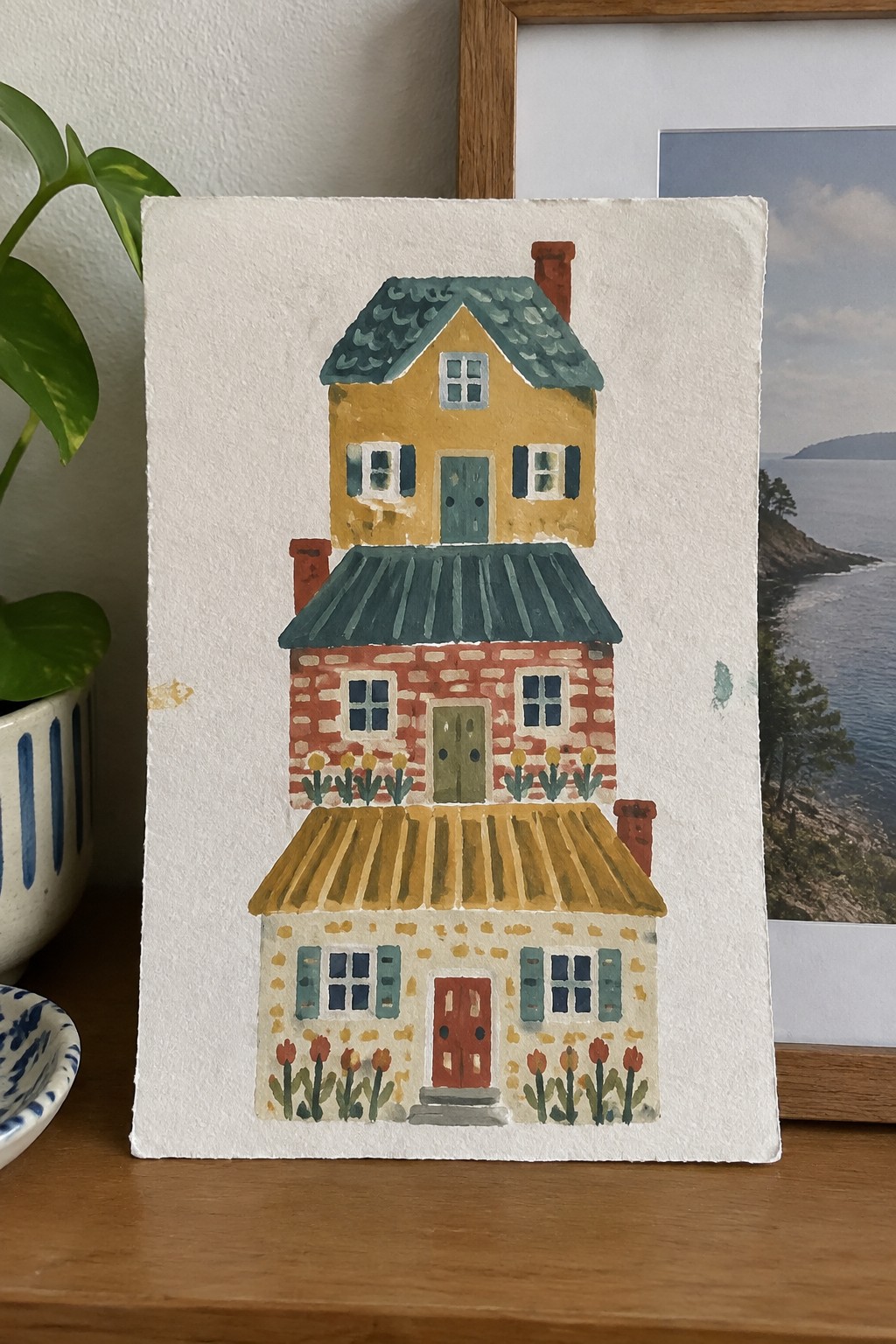 Watercolor of colorful three-story house with green roofs, flowers, and chimneys