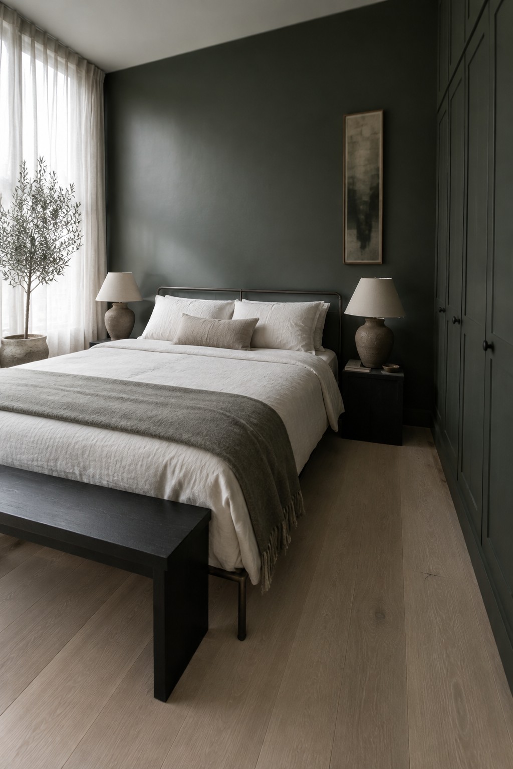 Minimalist bedroom with white linens, gray throw, dark green walls, and wooden floor.