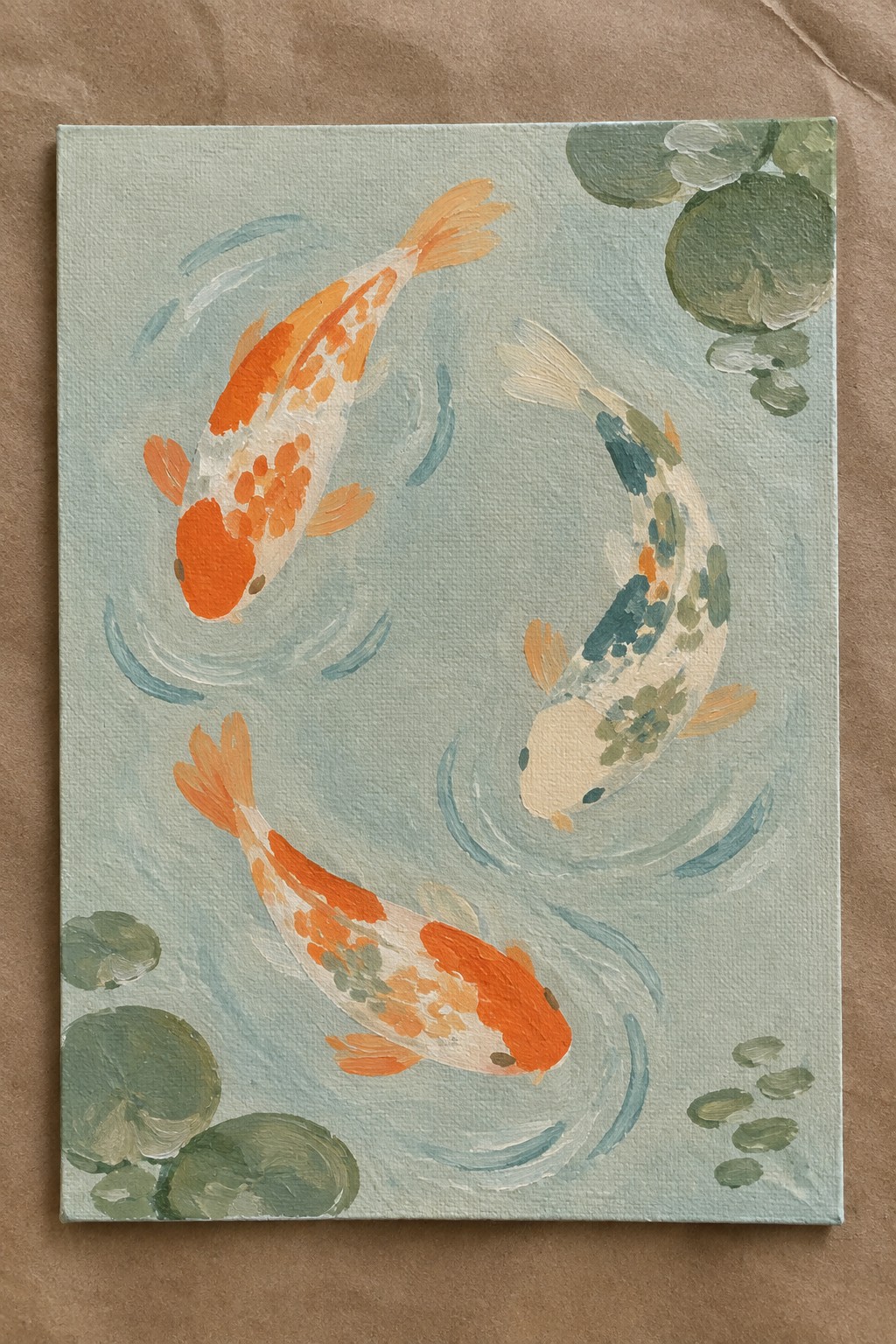 Three colorful koi fish swim in light blue water with green lily pads