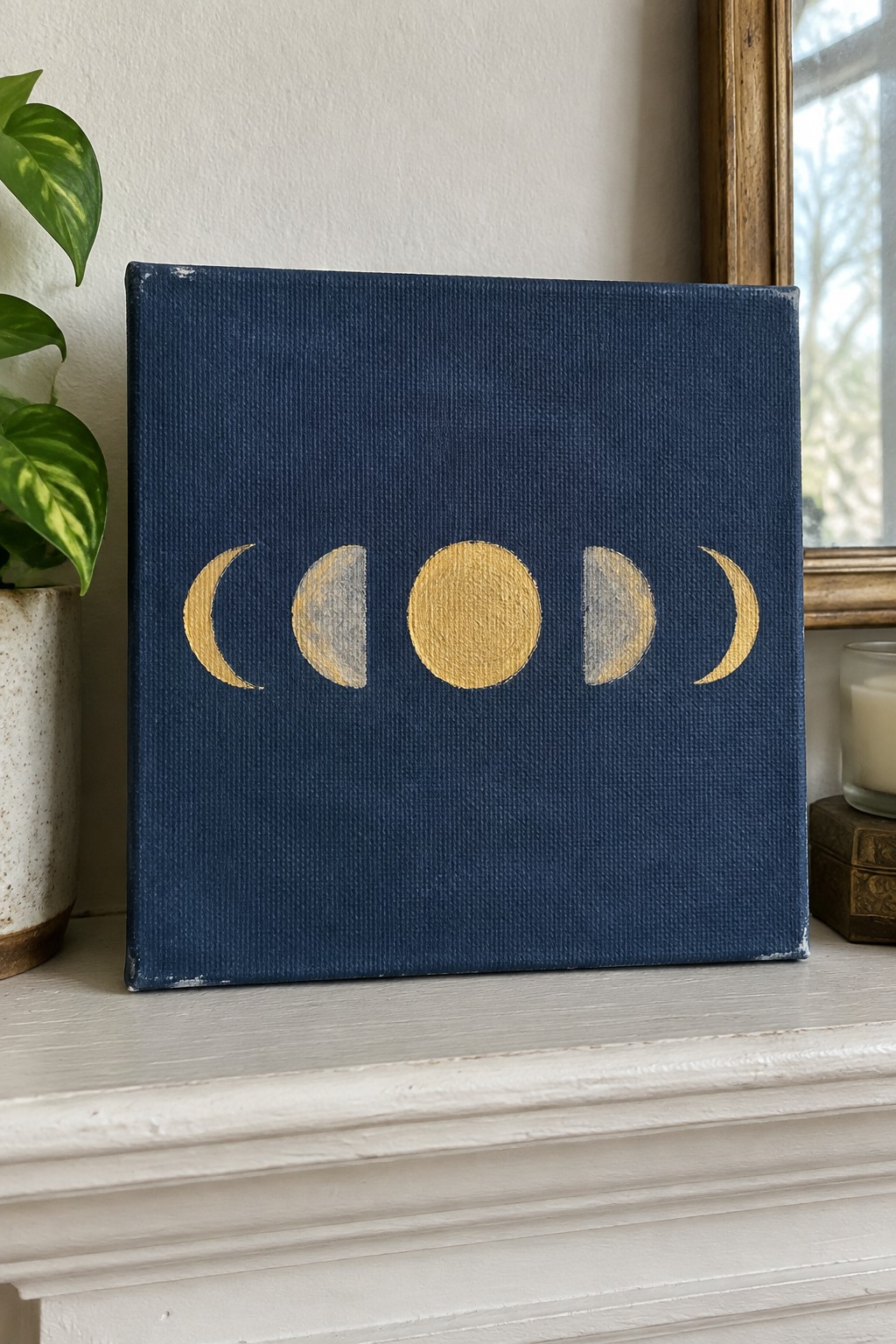 A dark blue canvas with five gold moon phases painted in a horizontal row.