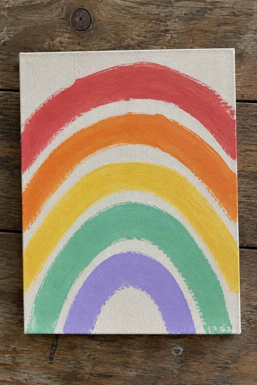 Rainbow painting in red, orange, yellow, green, purple on white canvas atop wood.