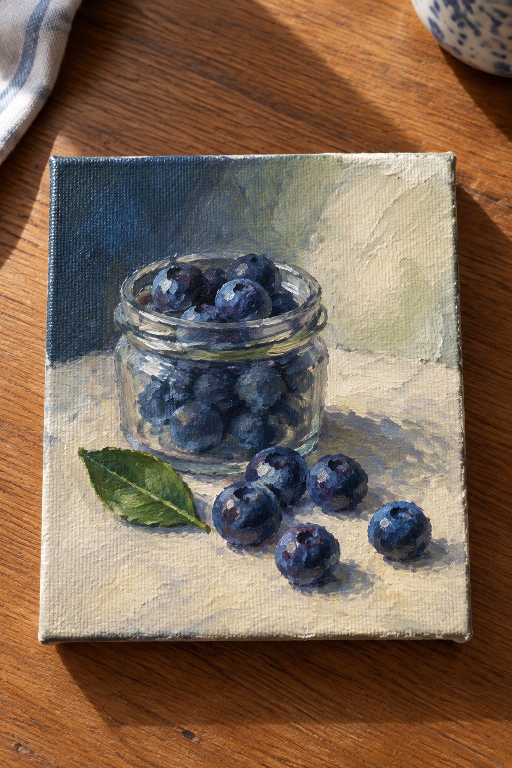 Oil painting of blueberries in glass jar with loose berries and leaf on wood