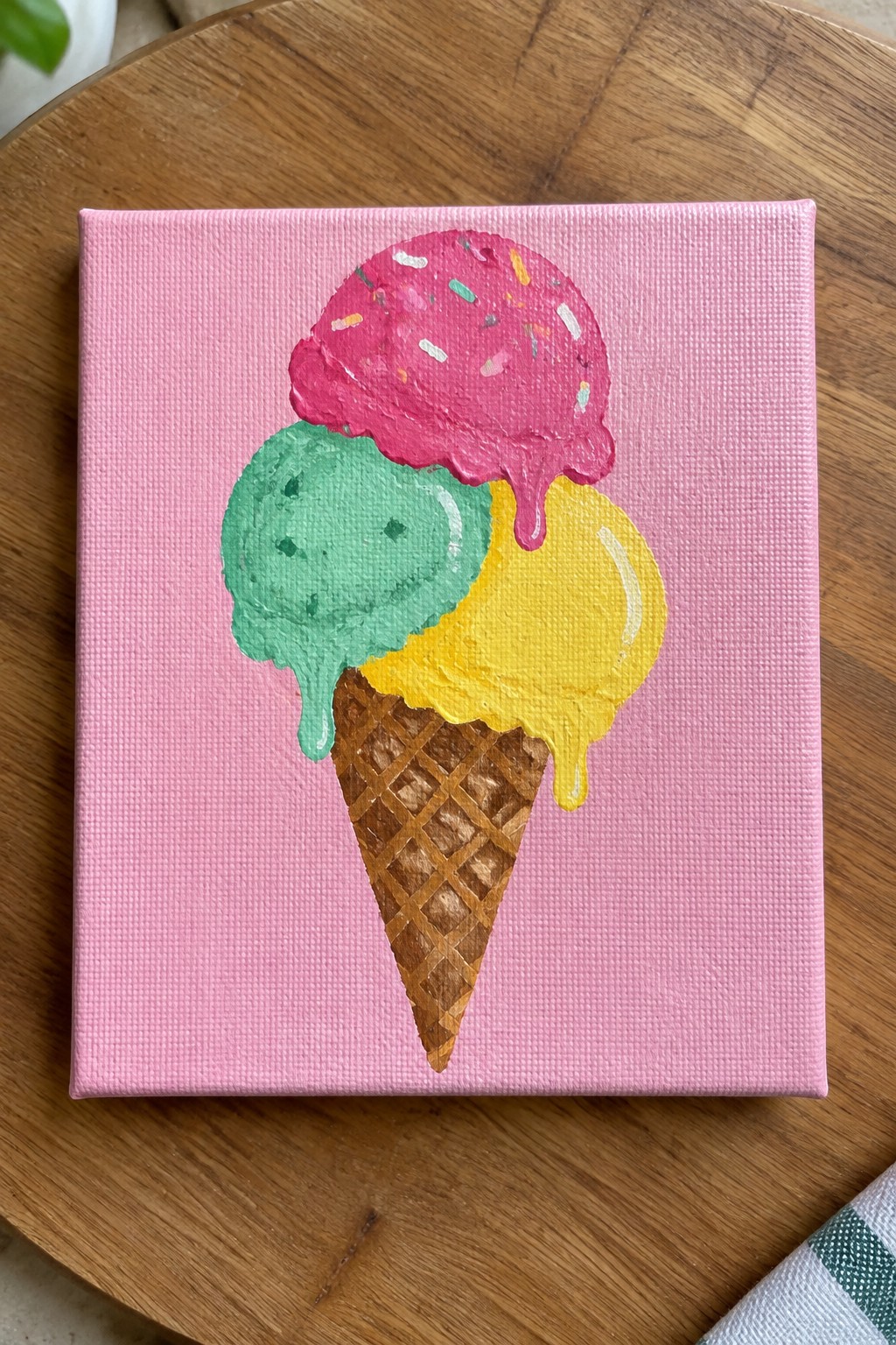 Melting pink, green, and yellow ice cream cone painted on pink canvas