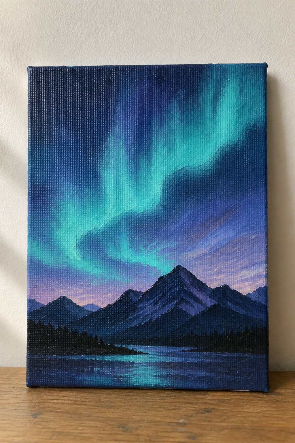 Acrylic painting of green aurora borealis over dark mountains and a glowing lake.