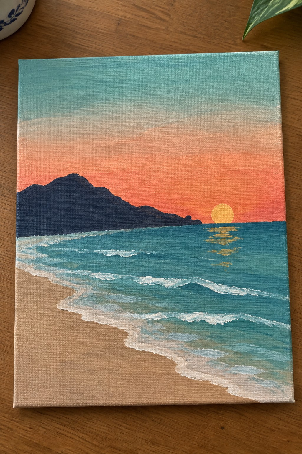 Sunset painting of turquoise waves on sandy beach with dark mountain silhouette and glowing sun.