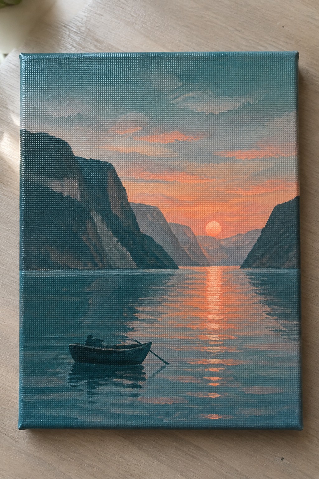 A small canvas painting shows a sunset over dark mountains with a boat on calm reflective water.