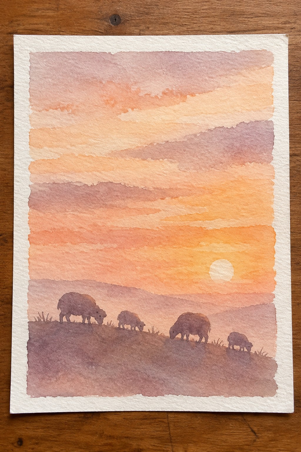 Watercolor sunset with four sheep grazing on a purple hillside under pink-orange sky.