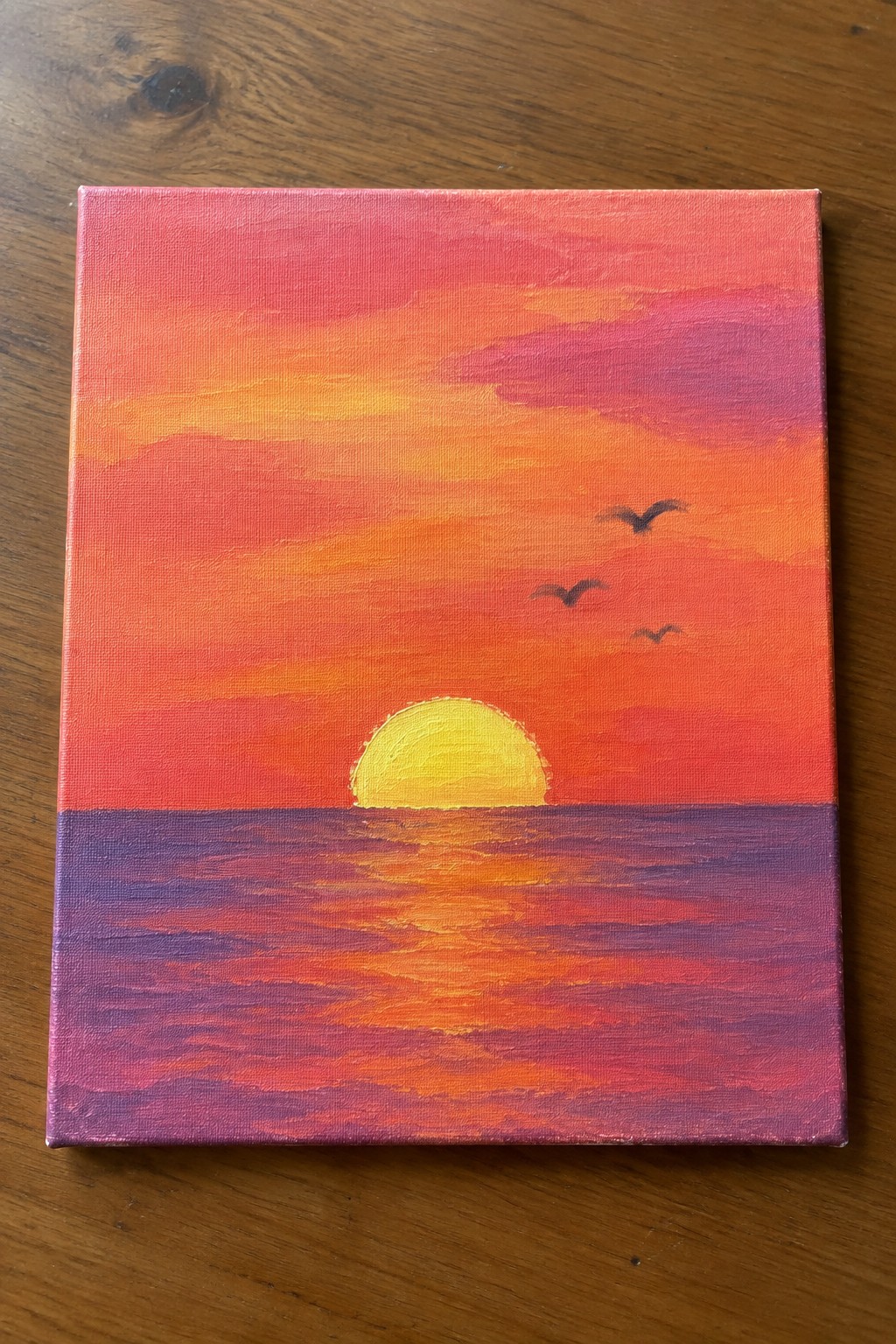 Vibrant sunset painting with yellow sun over orange-red sky, purple sea, and three birds